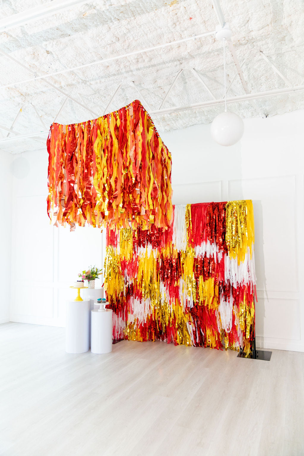 Fire Frenzy Aerial fringe garland hanging against a white wall with balloons. Fringe decor perfect for corporate events or parties.