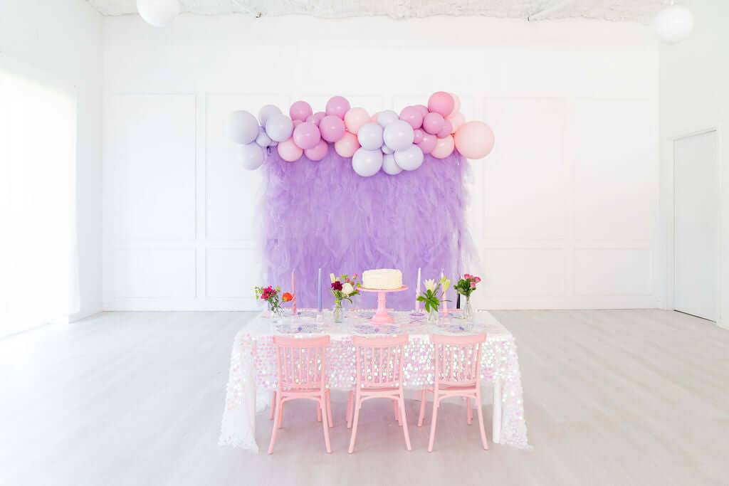 Elegant pink and purple party setup featuring balloons, flowers, and a beautifully decorated table for girls' celebration.