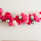 Pink Doll Balloon Kit fringe garland hanging against a white wall with balloons. Fringe decor perfect for corporate events or parties.