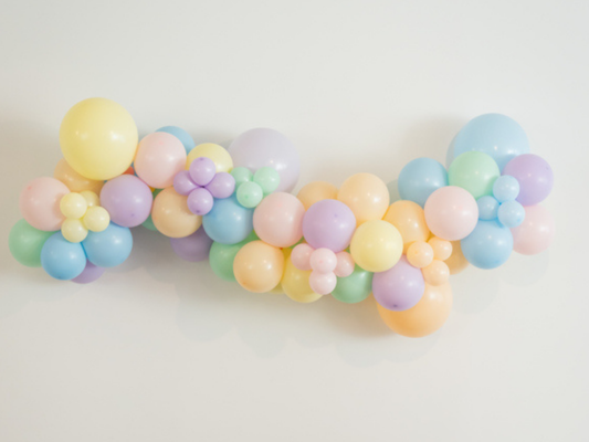 Pastel Balloon Kit fringe garland hanging against a white wall with balloons. Fringe decor perfect for corporate events or parties.