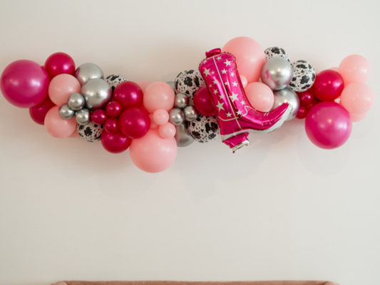 Pink Cowgirl Balloon Kit fringe garland hanging against a white wall with balloons. Fringe decor perfect for corporate events or parties.