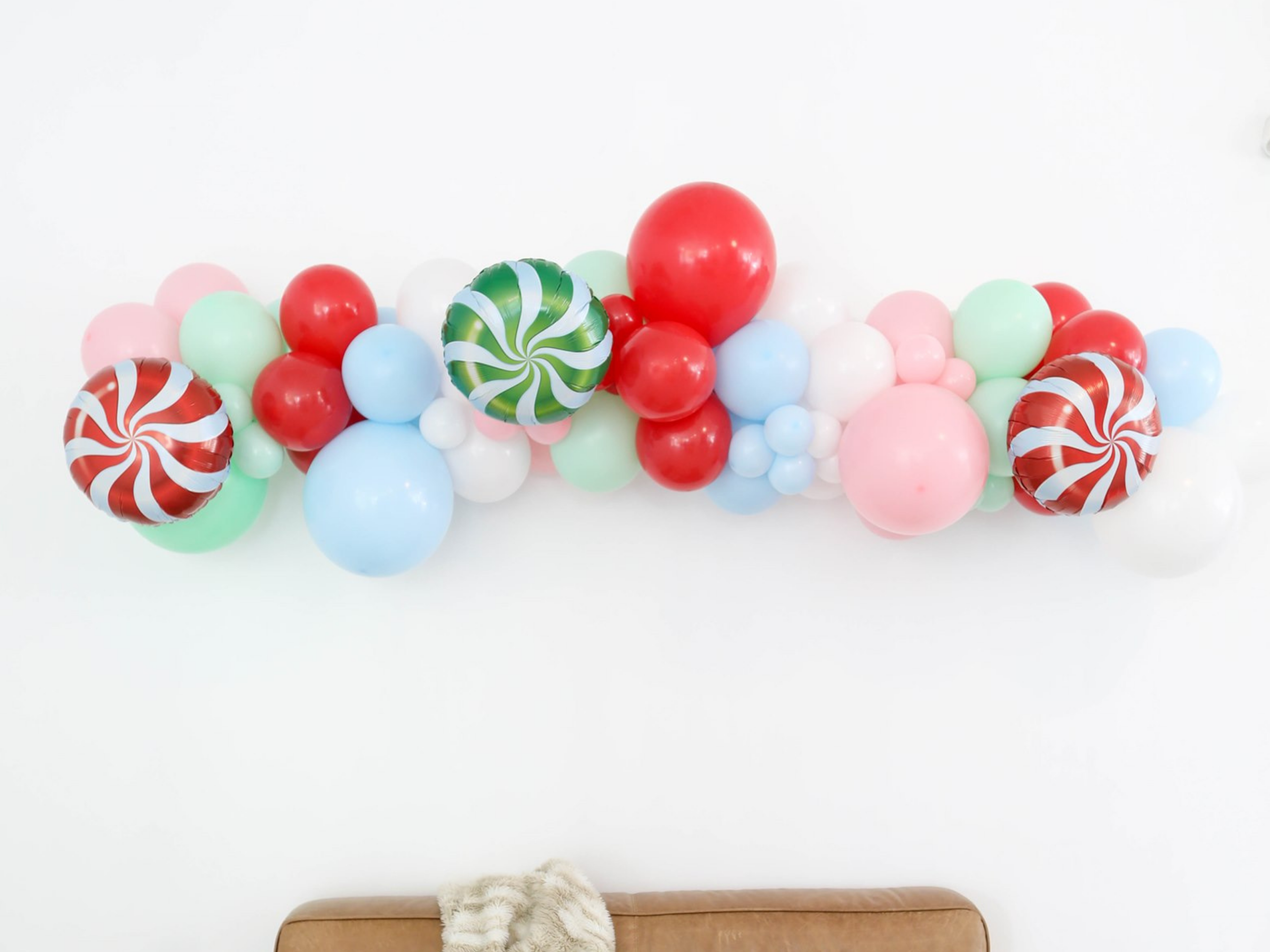 Merry & Bright Balloon Kit fringe garland hanging against a white wall with balloons. Fringe decor perfect for corporate events or parties.