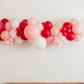 Pink Perfection Balloon Kit fringe garland hanging against a white wall with balloons. Fringe decor perfect for corporate events or parties.