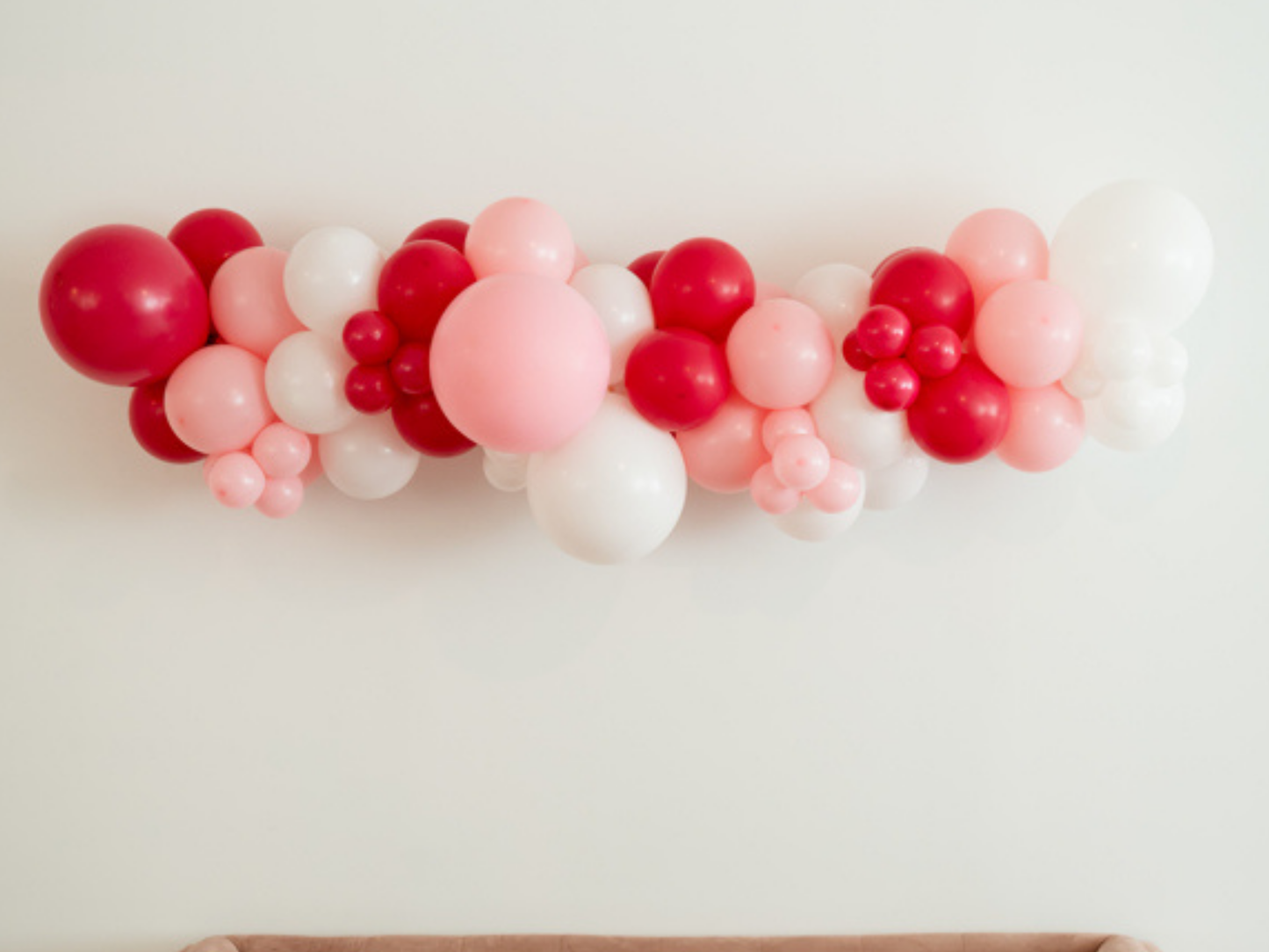 Pink Perfection Balloon Kit fringe garland hanging against a white wall with balloons. Fringe decor perfect for corporate events or parties.