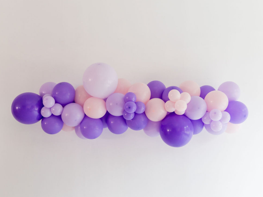 Lavender & Blush Balloon Kit fringe garland hanging against a white wall with balloons. Fringe decor perfect for corporate events or parties.