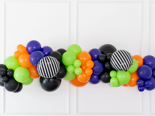 Spooky Time Balloon Kit fringe garland hanging against a white wall with balloons. Fringe decor perfect for corporate events or parties.