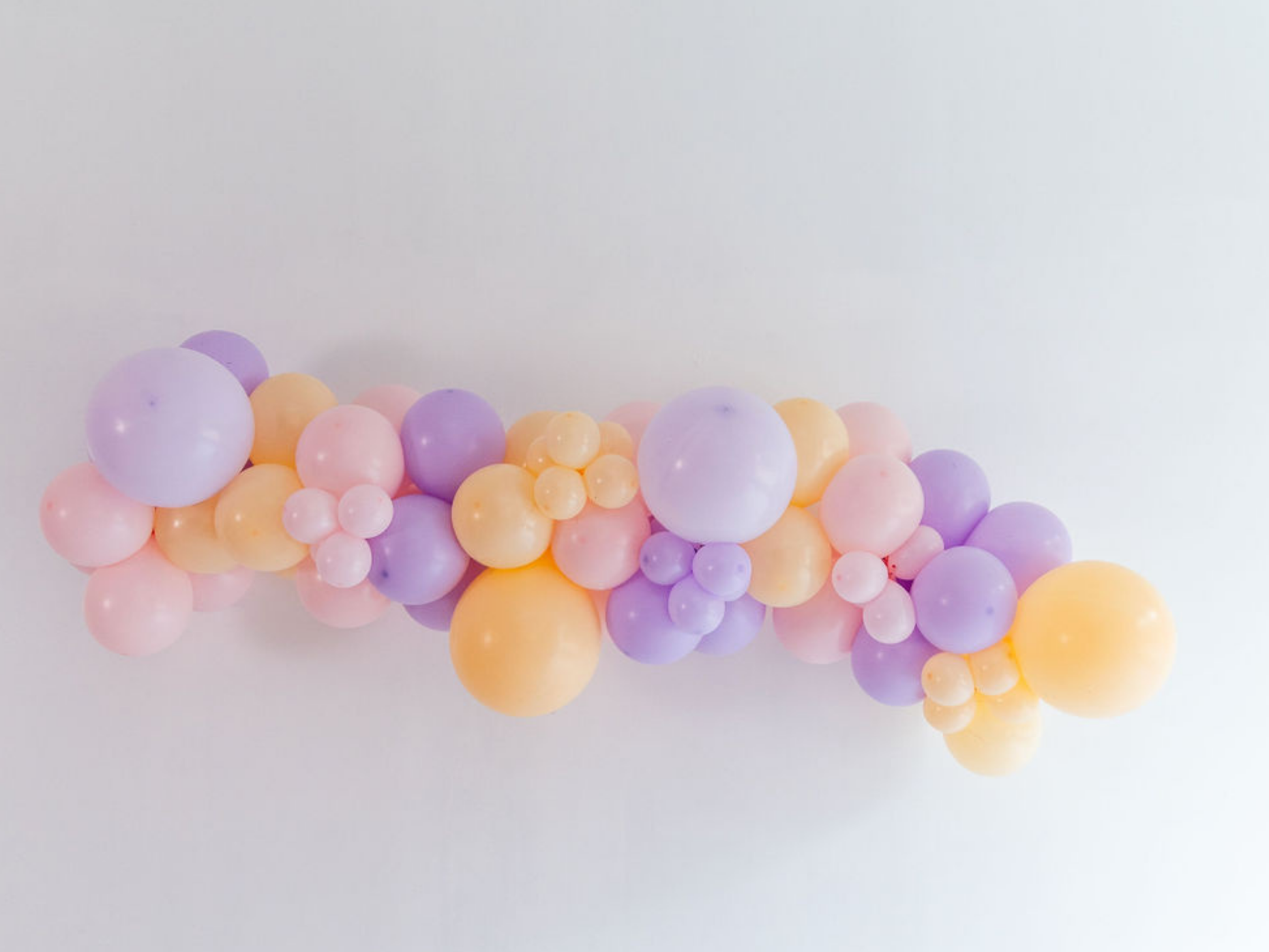 Sunset Splash Balloon Kit fringe garland hanging against a white wall with balloons. Fringe decor perfect for corporate events or parties.