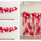 Pink Doll Balloon Kit fringe garland hanging against a white wall with balloons. Fringe decor perfect for corporate events or parties.