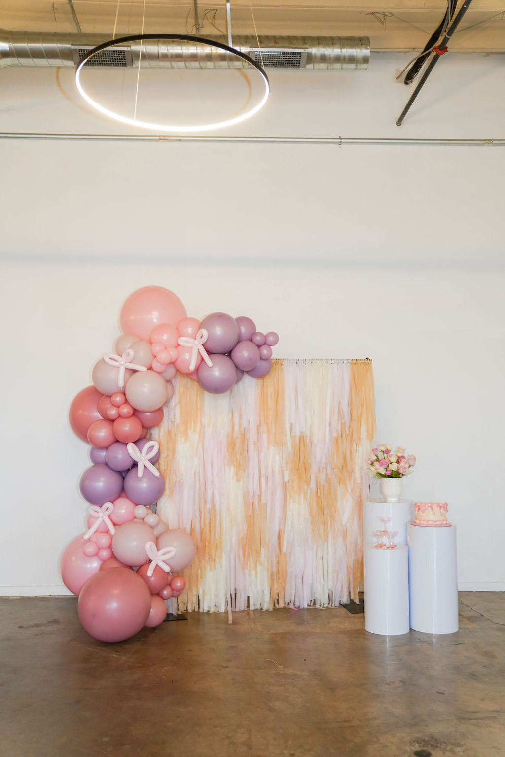 Bashful Blossoms Backdrop fringe garland hanging against a white wall with balloons. Fringe decor perfect for corporate events or parties.