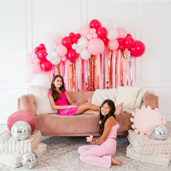 Teen girls in front of disco balls and pink and gold fringe backdrop and balloon garland by Oh My Darling Party Co