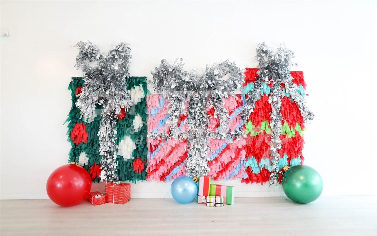 Present Shape Fringe Backdrop fringe garland hanging against a white wall with balloons. Fringe decor perfect for corporate events or parties.