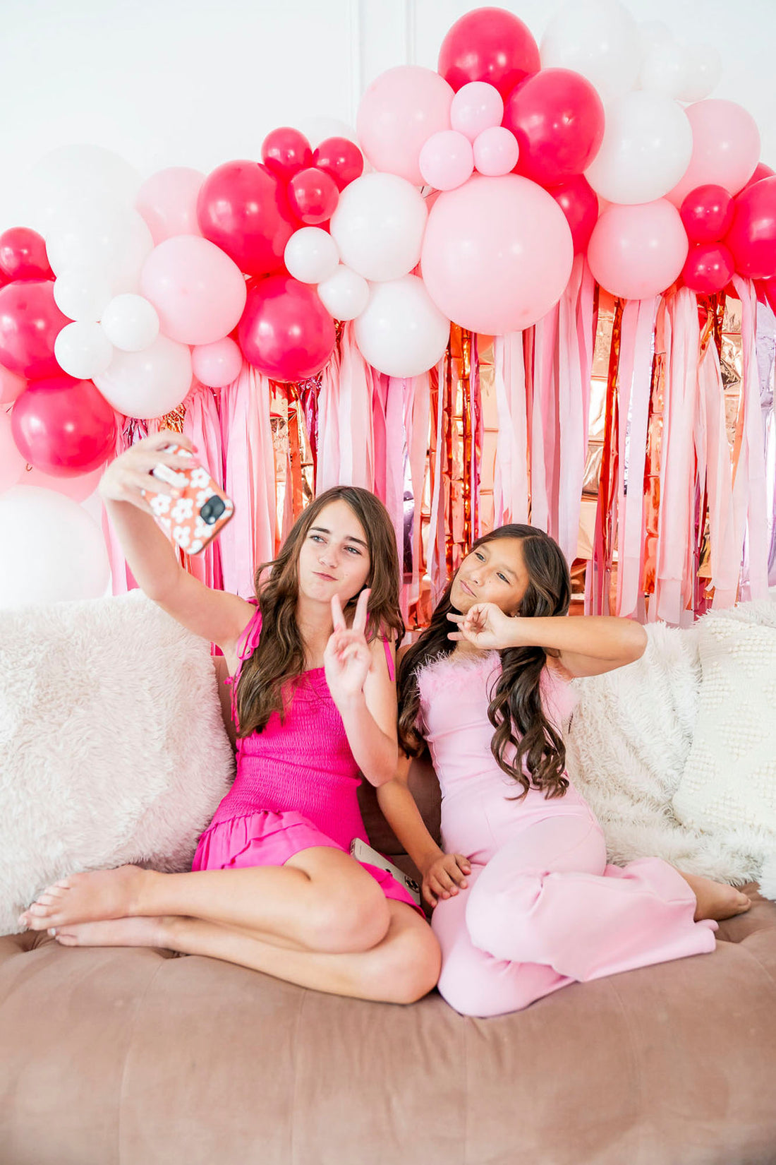 Girls taking selfie in front of pink fringe backdrop and balloon garland by Oh My Darling Party Co